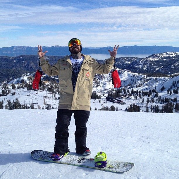 Sixer snowboarding at a mountain summit, arms raised